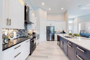 A modern kitchen with white cabinets, stainless steel appliances, and a tiled backsplash. - Brand-new home with pool, pool spa, grill, & screened-in patio - snowbirds OK (Marco Island)