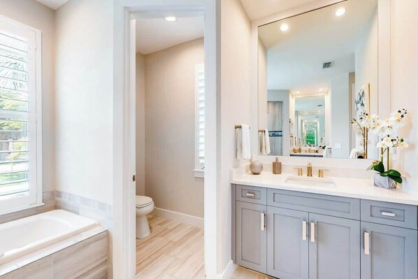 A bathroom with a bathtub, toilet, vanity with a mirror, and a window. - Brand-new home with pool, pool spa, grill, & screened-in patio - snowbirds OK (Marco Island)