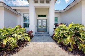 A building entrance with a double door, a small set of steps, and symmetrical landscaping with palm plants. - Brand-new home with pool, pool spa, grill, & screened-in patio - snowbirds OK (Marco Island)