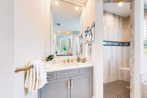 A modern bathroom with a large mirror, a sink, and a shower area. - Brand-new home with pool, pool spa, grill, & screened-in patio - snowbirds OK (Marco Island)