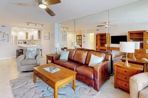 A modern living room with a sofa, coffee table, and a large mirror reflecting the space. - Waterfront condo with bay views, pool, tennis, pickleball, beach, & dock access (Marco Island)