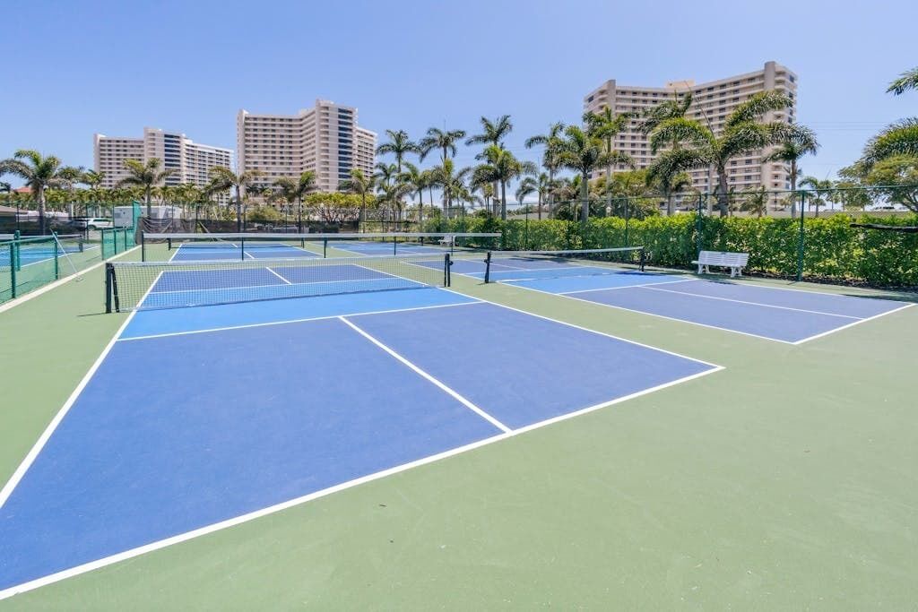 Canchas de tenis múltiples, rodeadas de palmeras y edificios al fondo.