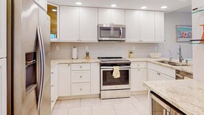 Een moderne keuken met witte kastjes, roestvrijstalen apparatuur en een marmeren aanrecht.