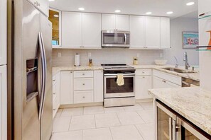 A modern kitchen with white cabinets, stainless steel appliances, and a marble countertop. - Waterfront condo with bay views, pool, tennis, pickleball, beach, & dock access (Marco Island)
