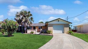 A single-story house with a garage, a well-maintained lawn, and a palm tree. - Waterfront home with, private grill, and washer and dryer, and Gulf access (Fort Myers Beach)