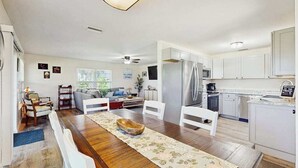 A spacious living area with a wooden dining table, white chairs, a sofa, and a kitchen with white cabinets and appliances. - Waterfront home with, private grill, and washer and dryer, and Gulf access (Fort Myers Beach)