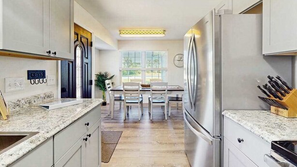 A kitchen with a granite countertop, stainless steel appliances, a dining area with a table and chairs, and a window with blinds. - Waterfront home with, private grill, and washer and dryer, and Gulf access (Fort Myers Beach)