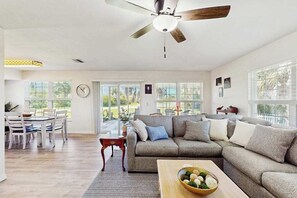 Ein geräumiges Wohnzimmer mit Ecksofa, Esstisch und Stühlen, großen Fenstern und Deckenventilator.