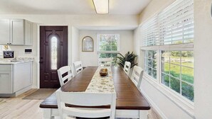 A dining area with a long table, chairs, a dark wooden table runner, and a view through large windows. - Waterfront home with, private grill, and washer and dryer, and Gulf access (Fort Myers Beach)