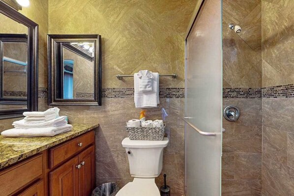 A bathroom with a toilet, a sink with a towel stack, a mirror, and a shower area.