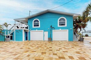 A two-story house with a blue exterior, two garage doors, a covered porch, and a paved driveway.