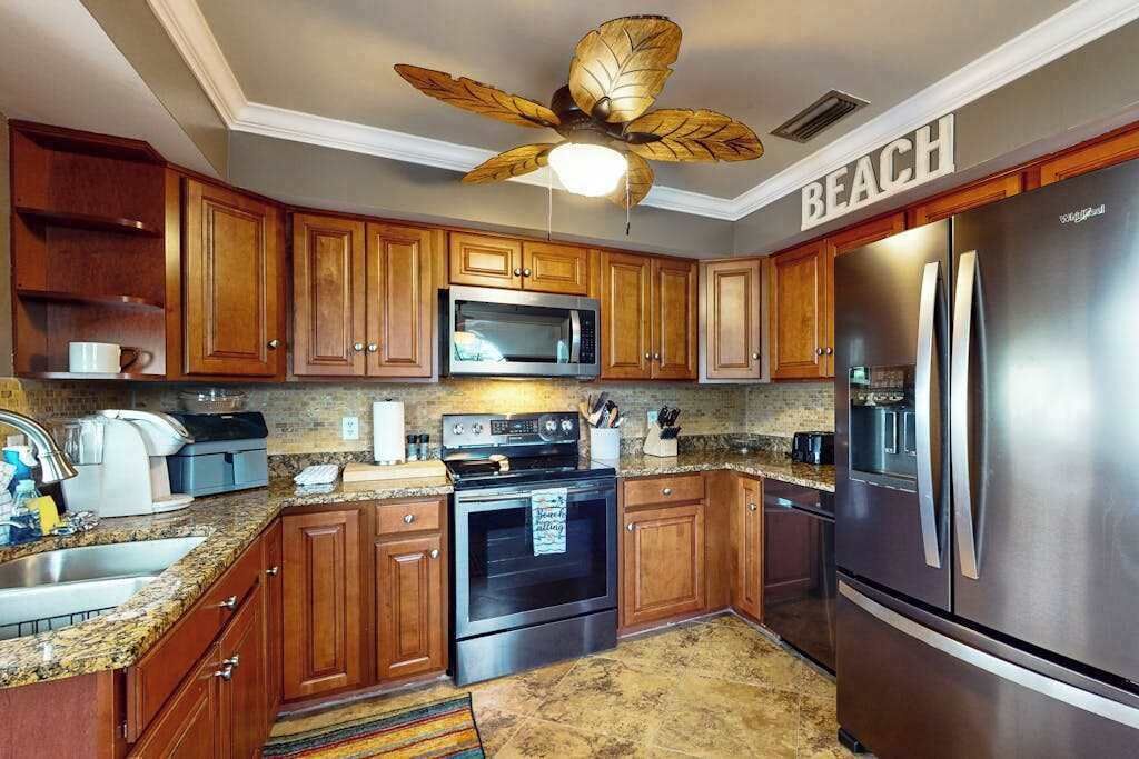 A kitchen with wooden cabinets, a stainless steel refrigerator, a microwave, an oven, and a ceiling fan.