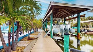 A covered dock area with boats, palm trees, and a pool. - Spacious home with heated pool, lots of outdoor entertainment, and WIFI (Fort Myers Beach)