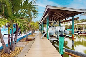 A covered dock area with boats, palm trees, and a pool.