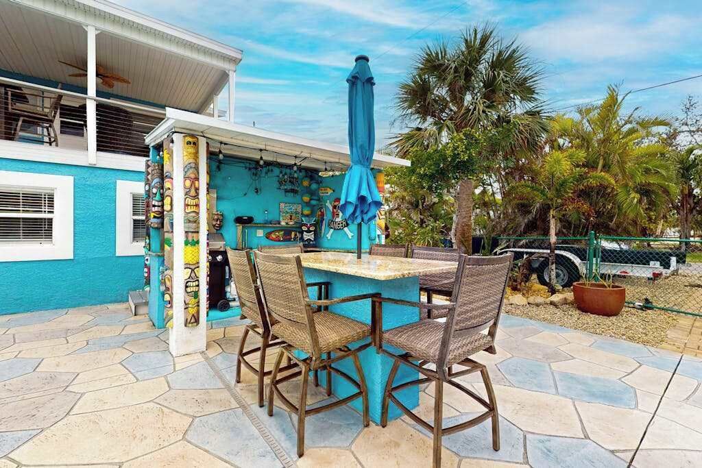 Un'area bar all'aperto con decorazioni tiki, un ombrello blu e sedie in vimini.