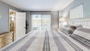 A bedroom with a bed, a dresser, a lamp, and a view of the outside. - Spacious home with heated pool, lots of outdoor entertainment, and WIFI (Fort Myers Beach)