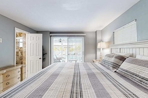 A bedroom with a bed, a dresser, a lamp, and a view of the outside.