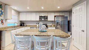 A kitchen with white cabinets, a granite countertop, a stainless steel refrigerator, and a microwave. - Spacious home with heated pool, lots of outdoor entertainment, and WIFI (Fort Myers Beach)