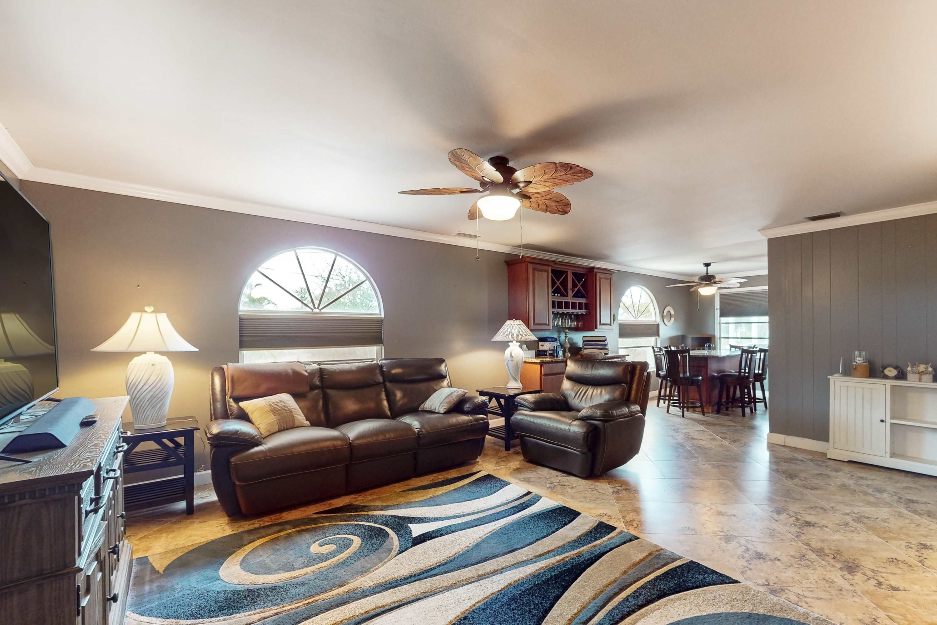 A living room with a sofa, armchairs, a coffee table, a rug, a lamp, and a ceiling fan.