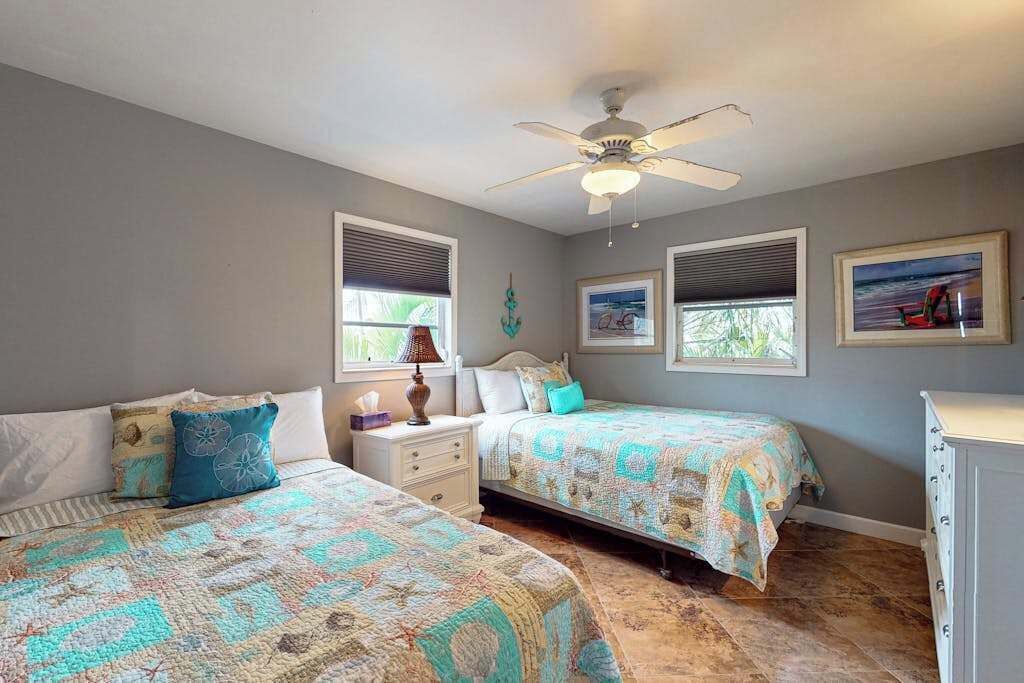 A bedroom with two beds, a ceiling fan, and two windows with blinds.
