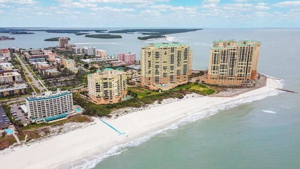 A coastal cityscape with high-rise buildings, a beach, and a marina. - Beachfront condo with huge lanai, sunset gulf views, pool, hot tub, tennis & gym (Marco Island)