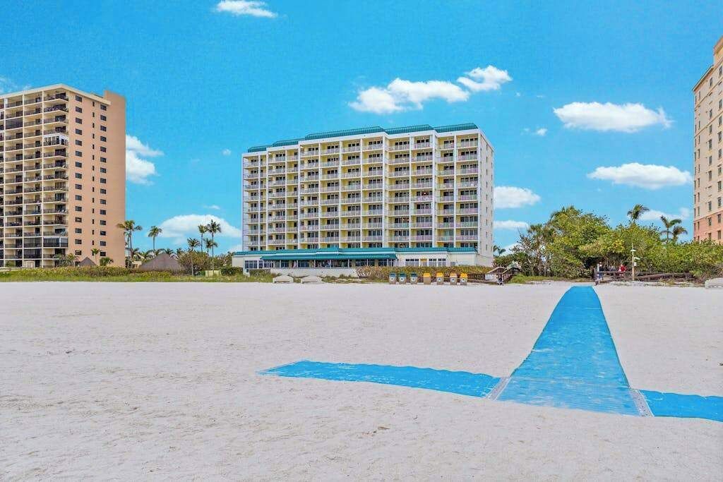A beachfront hotel with multiple floors, a blue pathway, and palm trees.