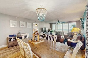 Ein Essbereich mit Holztisch, Stühlen, einer Chandelüster und Blick auf den Ozean durch große Fenster.