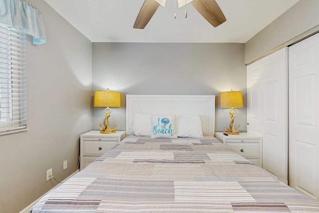 A bedroom with a bed, two bedside tables with lamps, a headboard, and a window with blinds.