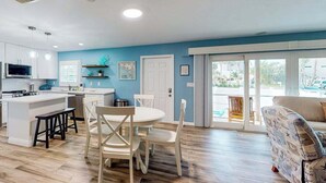 A modern kitchen with white cabinets, a central island, and a dining area with a round table and white chairs. - Bright & breezy beach house with private pool, sunroom, washer/dryer, & AC (Fort Myers Beach)