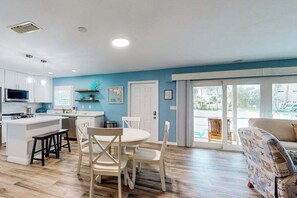 A modern kitchen with white cabinets, a central island, and a dining area with a round table and white chairs. - Bright & breezy beach house with private pool, sunroom, washer/dryer, & AC (Fort Myers Beach)