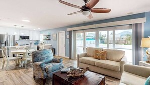 A modern living room with a ceiling fan, a sofa, a coffee table, and a view of the outside. - Bright & breezy beach house with private pool, sunroom, washer/dryer, & AC (Fort Myers Beach)