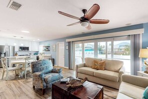 A modern living room with a ceiling fan, a sofa, a coffee table, and a view of the outside. - Bright & breezy beach house with private pool, sunroom, washer/dryer, & AC (Fort Myers Beach)