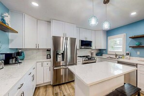 A modern kitchen with white cabinetry, stainless steel appliances, and a central island. - Bright & breezy beach house with private pool, sunroom, washer/dryer, & AC (Fort Myers Beach)