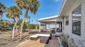 A covered patio with outdoor furniture, palm trees, and a house with a large window. - Updated tropical home with a private patio, beach gear, AC, and washer/dryer (Marco Island)