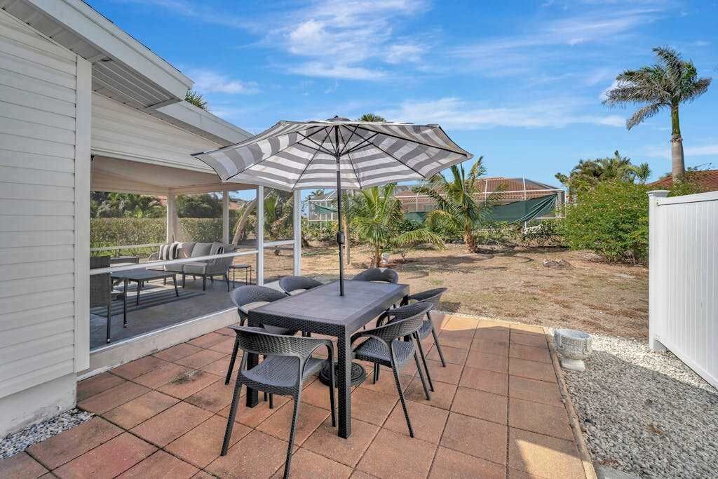 Un patio con una mesa y sillas, un paraguas a rayas y una zona de estar cubierta.