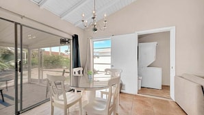 A dining area with a glass table and chairs, a chandelier, a sliding glass door leading outside, and a white sofa. - Updated tropical home with a private patio, beach gear, AC, and washer/dryer (Marco Island)
