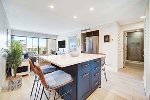 A modern kitchen with a central island, bar stools, and a dining area with a sofa and coffee table. - Remodeled condo in a waterfront complex with pools, hot tubs, & tennis (Marco Island)