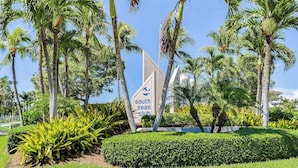 Une enseigne indiquant l’entrée du South Seas Club, entourée de palmiers et de haies bien entretenues.