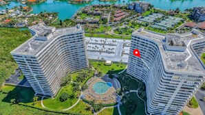 Un hôtel de grande hauteur doté d’une piscine centrale, entouré d’une végétation luxuriante et d’un port de plaisance.
