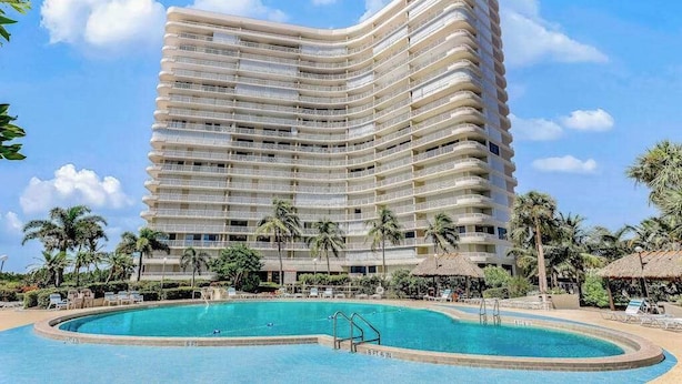 Un hôtel à plusieurs étages doté d’une piscine, de palmiers et offrant une vue sur un ciel dégagé.