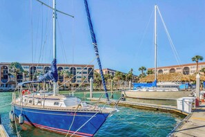 A marina with boats docked, a building with arched windows, and palm trees in the background. - Snowbird-friendly condo with AC, lanai, pool, hot tub, tennis, & on-site dining (Marco Island)