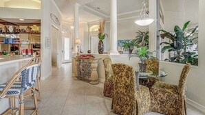 A spacious living area with a high ceiling, a dining table with chairs, and a kitchen area visible in the background. - Waterfront home with saltwater pool, pool spa, central AC, W/D, & office space (Marco Island)
