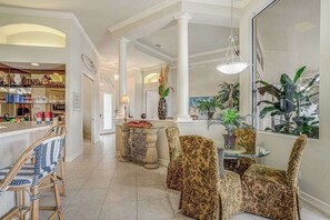 A spacious living area with a high ceiling, a dining table with chairs, and a kitchen area visible in the background. - Waterfront home with saltwater pool, pool spa, central AC, W/D, & office space (Marco Island)