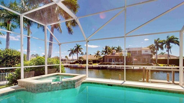 A pool with a glass enclosure, surrounded by palm trees and a view of a body of water. - Waterfront home with saltwater pool, pool spa, central AC, W/D, & office space (Marco Island)