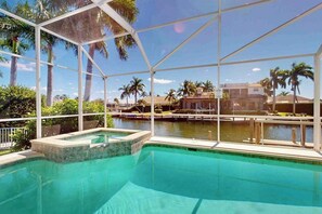 Piscina com estrutura de vidro, rodeada por palmeiras e vista para um corpo de água.