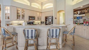 A spacious kitchen with high ceilings, built-in cabinets, a central island with bar stools, and a refrigerator. - Waterfront home with saltwater pool, pool spa, central AC, W/D, & office space (Marco Island)