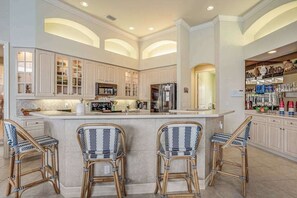 A spacious kitchen with high ceilings, built-in cabinets, a central island with bar stools, and a refrigerator. - Waterfront home with saltwater pool, pool spa, central AC, W/D, & office space (Marco Island)
