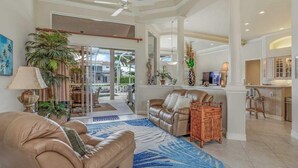 A spacious living area with a leather sofa, a coffee table, and a large window. - Waterfront home with saltwater pool, pool spa, central AC, W/D, & office space (Marco Island)