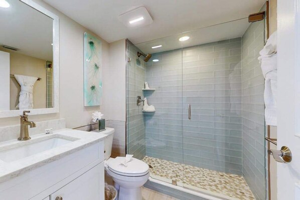 Un baño con cabina de ducha de vidrio, un lavabo blanco y un inodoro.