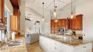A kitchen with granite countertops, wooden cabinets, and pendant lighting. - Large corner lot home with canal views & screened in pool - close to the beach (Marco Island)